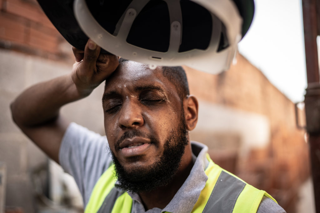 Photograph of a man in the heat, sweating and rubbing his brow. 